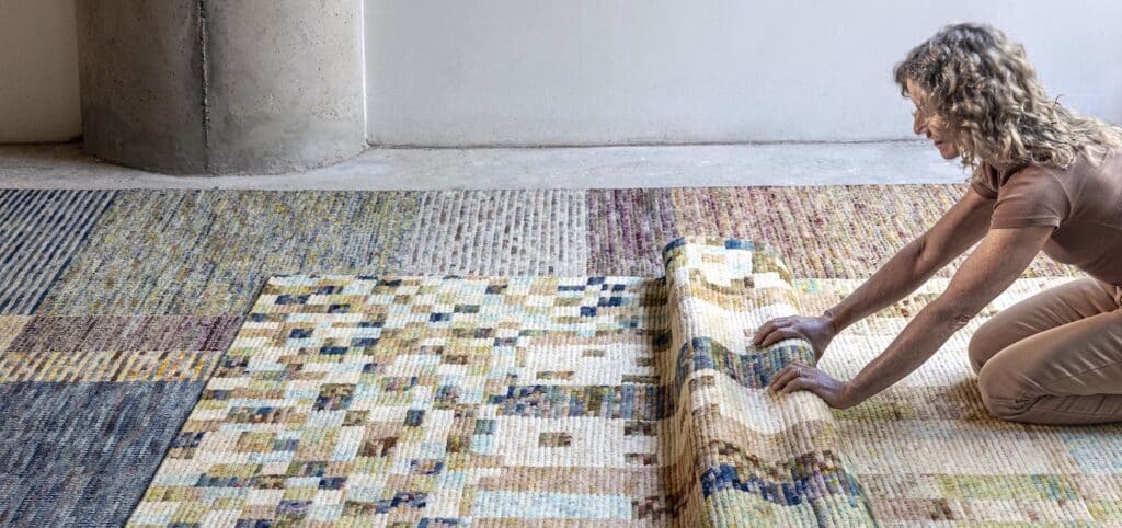 Mujer desenrollando una alfombra de diseño geométrico en tonos pastel sobre otras alfombras