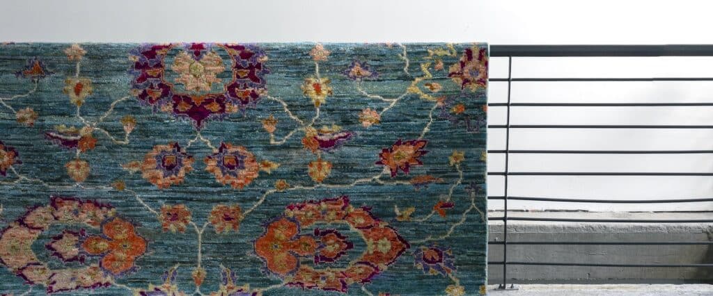 Alfombra anudada a mano de fondo turquesa con motivos florales naranjos y morados