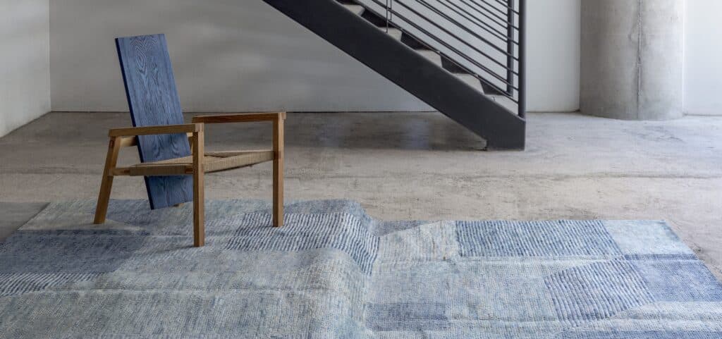 Alfombra azul de diseño contemporáneo frente a una silla de madera y una escalera, en un espacio de cemento